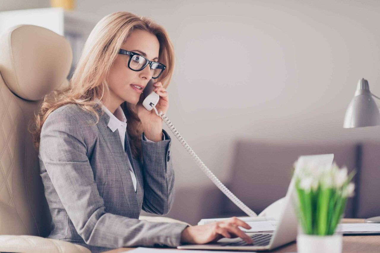A professional at a desk multitasking on a laptop and phone call.